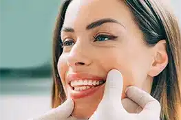 Smiling woman receiving dental examination with dentist's gloved hands checking teeth near beach setting.