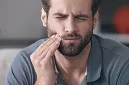 Man with hand to cheek experiencing dental pain or discomfort indoors.
