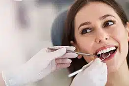 Smiling woman receiving dental examination from dentist wearing white gloves in clinical setting.