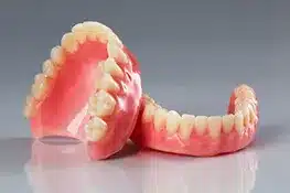 Dental prosthetics displaying pink dentures and teeth models on gray surface.