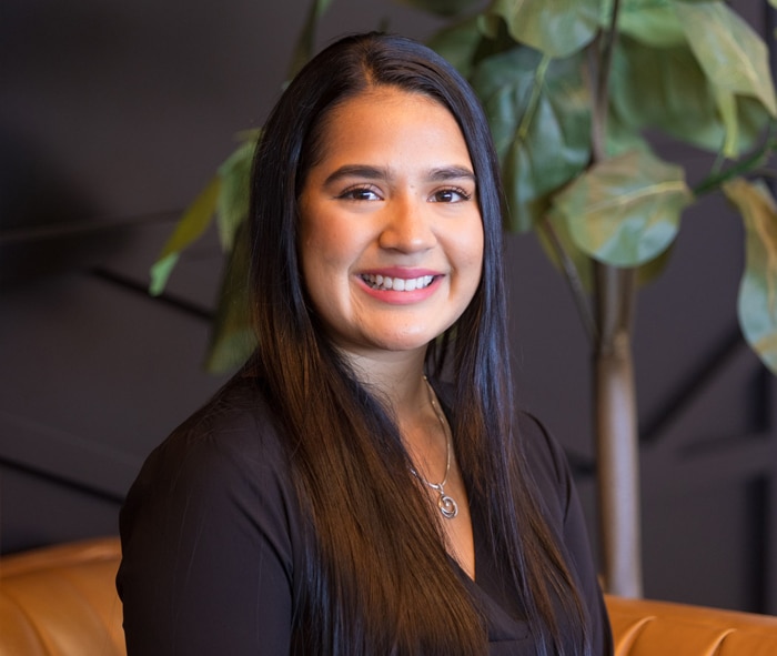 Woman smiling at camera in dental office setting with plant in background.