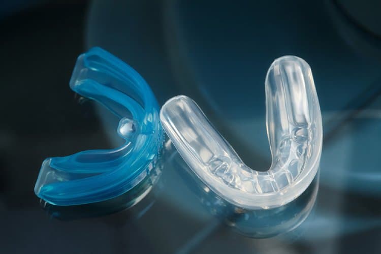 Two custom mouthguards, one blue and one clear, displayed against dark background with lighting effects.
