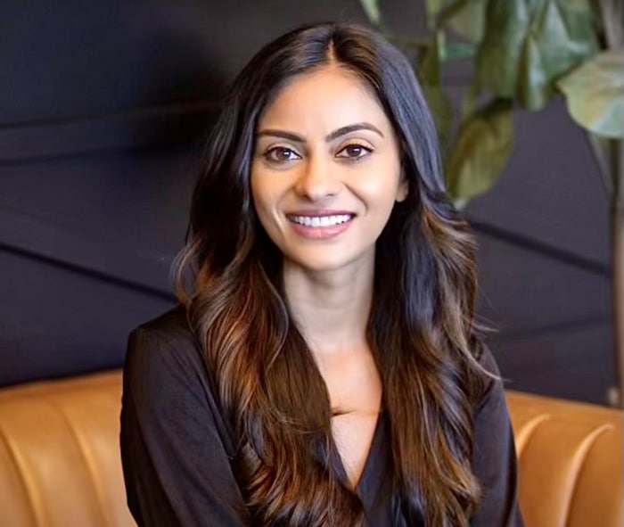 Woman smiling at camera, seated on orange couch in professional dental office setting.