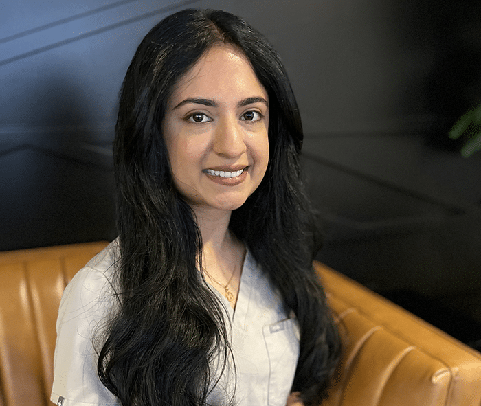 Woman with long dark hair smiling at camera, seated in dental office setting.