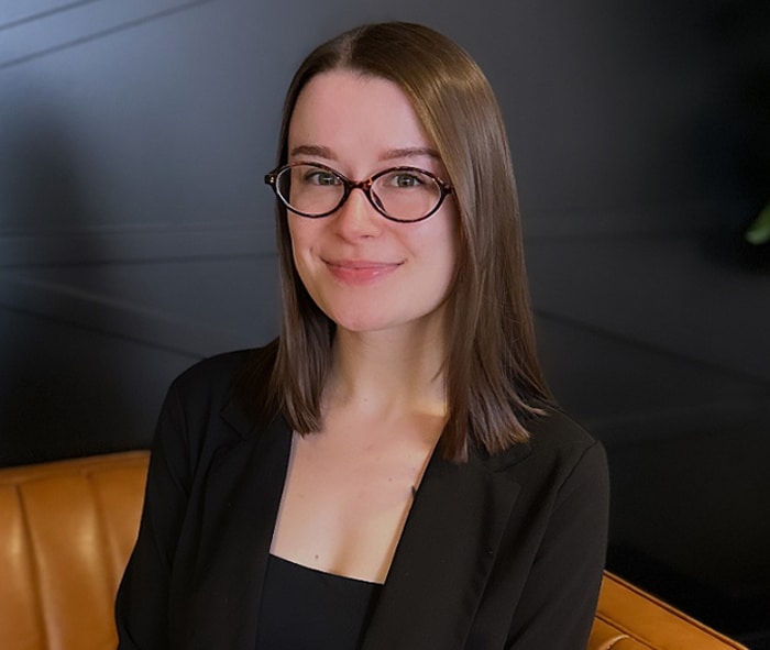 Woman with glasses wearing black blazer smiling at dental office.
