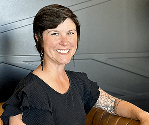 Woman smiling at camera in dental office wearing black shirt with arm tattoo