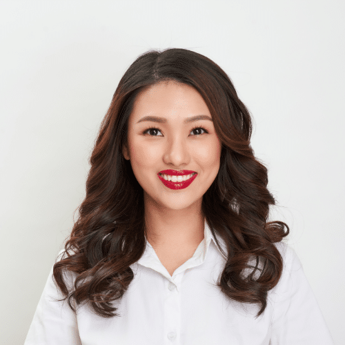 Professional headshot of woman with long dark wavy hair wearing white shirt against neutral background.