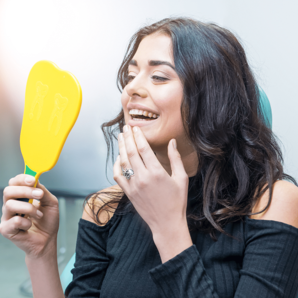 Woman holding yellow paddle, smiling and touching face, dental office setting.