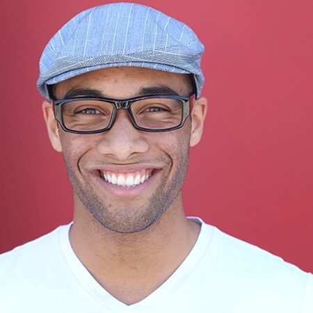 Smiling man wearing glasses and blue cap against red background.