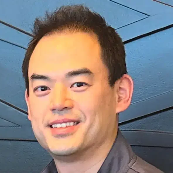 Professional headshot of smiling male dental professional against modern blue architectural background