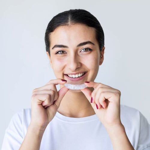 Smiling woman holding clear dental aligner tray against white background for dental center website.